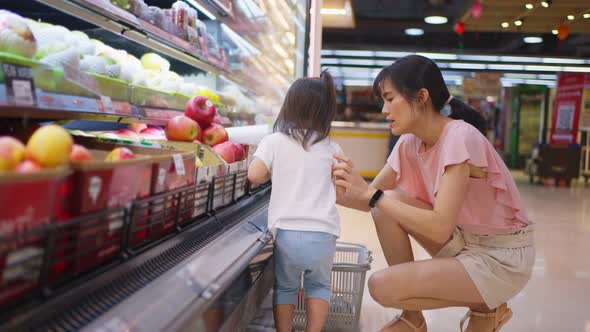 Asian young beautiful mother holding grocery basket with her little kid child walking in supermarket