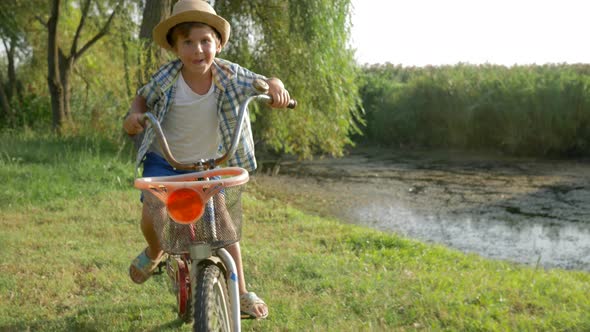 Little Boy Having Fun Riding His Bicycle in Countryside on Background of Lake and Nature