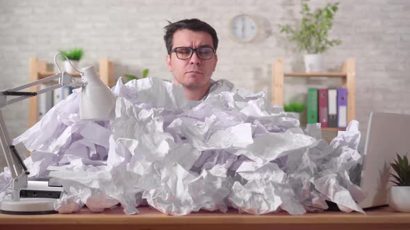 Perplexed Man Office Worker with Glasses in a Heaps of Paper on the Office Desk