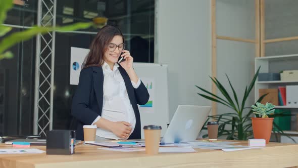 A Beautiful Pregnant Woman Talking on a Cell Phone Sitting at a Table