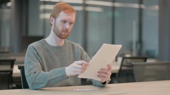 Young Man Reading Reports While Sitting in Office