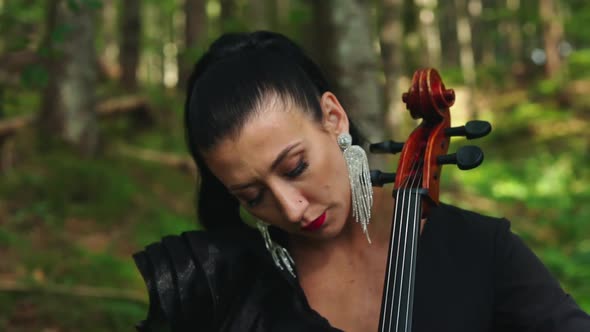 Woman with cello in the forest. Portrait of a dark-haired woman playing the musical instrument 