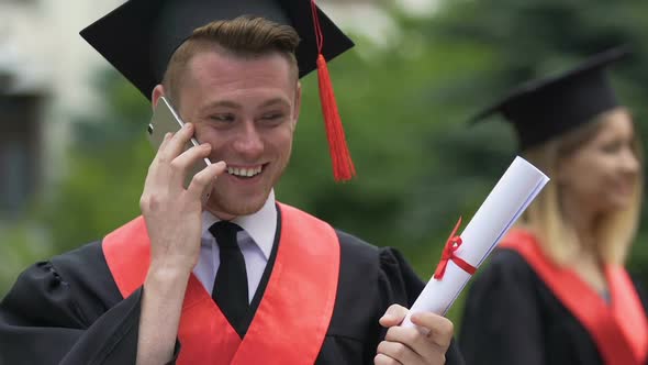 Smiling Male Graduating Student Holding University Diploma Talking on Phone