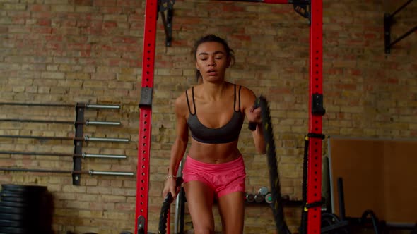 Motivated Fitness Black Female Doing Cross Training with Battle Ropes in Gym