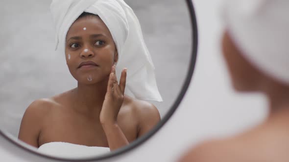 Happy african american woman apply cream on face in bathroom