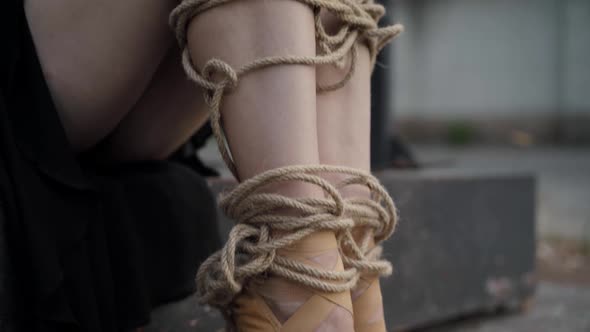 Camera Moves Up Along Legs of Slim Ballerina with Legs Tied with Ropes Hugging Knees