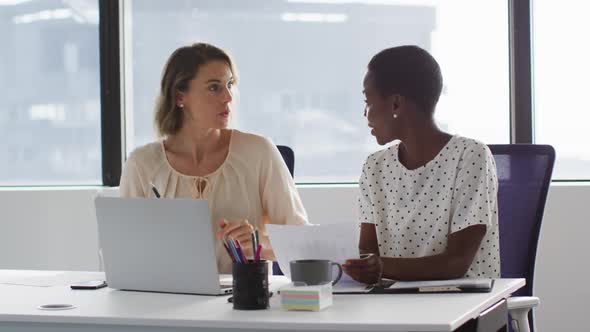 Two diverse female colleagues looking at laptop and discussing in office