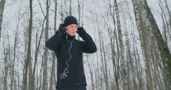 A Young Man on a Morning Jog Holds Headphones in His Hands and Inserts It Into His Ears Before
