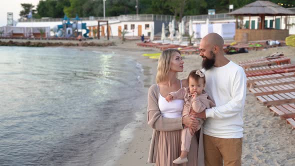 Happy Family Man Woman and Their Nursing Baby in Casual Clothes Hug Together at Sunrise Over the Sea