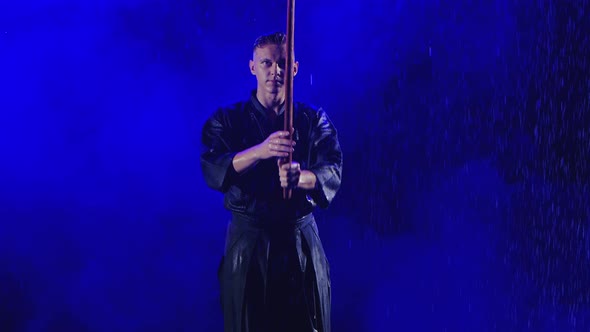 Exercise with a Wooden Sword of a Kendo Master in a Blue Kimono Under Streams of Rain. Shot in Slow