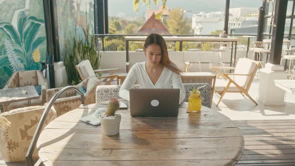 A Young Asian Girl Works at Her Laptop in a Rooftop Cafe in the City