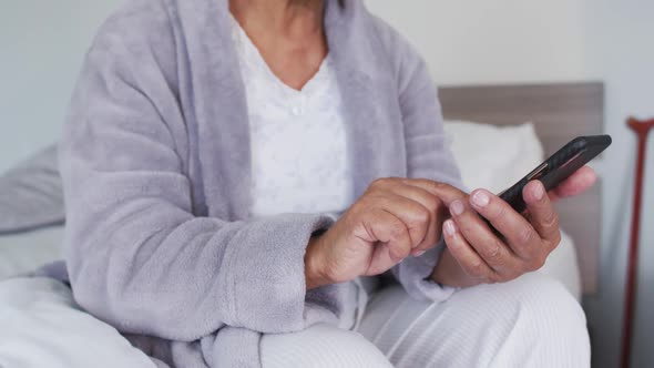 Mid section of african american senior woman using smartphone while sitting on the bed at home