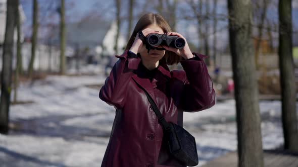 Portrait of Serious Woman with Binoculars Standing in Winter Park Looking Away