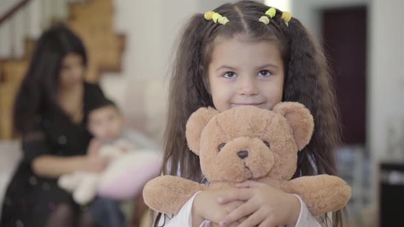 Close-up of a Smiling Middle Eastern Girl with Brown Eyes and Curly Hair Holding the Teddy Bear