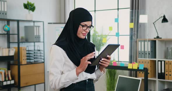 Muslim Woman in Traditional Headscarf Standing Sideways to the Camera in Modern Office