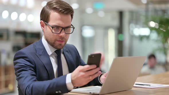 Businessman Using Smartphone and Laptop at Work 