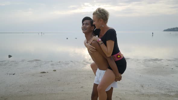 Lovely Interracial Couple Piggyback Ride and Kissing at the Beach at Sunset