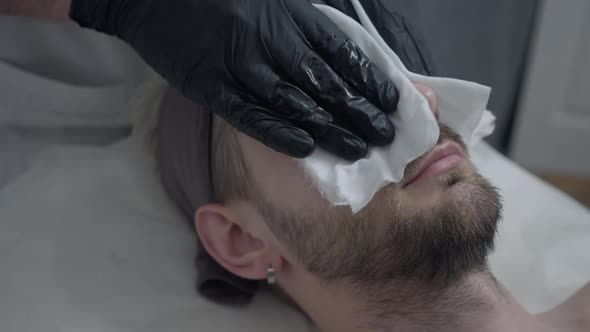 Closeup Male Beautician Hands in Gloves Wiping Face of Handsome Client in Beauty Parlor