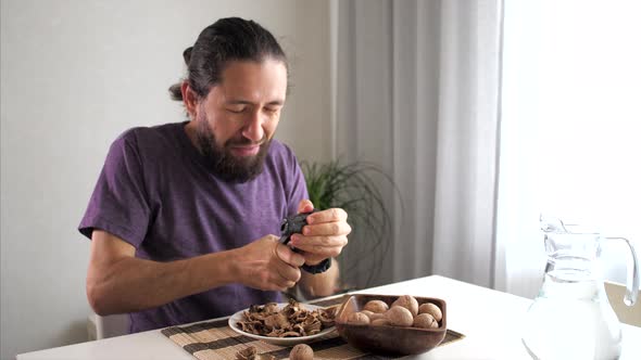 Young Bearded Man Is Cracking and Eating a Walnuts at Domestic Room