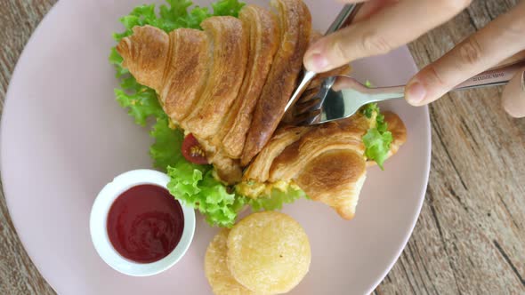 Top View of Woman Cutting Croissant Sandwich