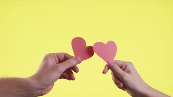 Close Up of Female and Male Hold in Hands Little Hearts Isolated on Yellow Background. Valentines