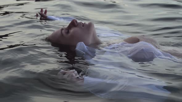 A Young Woman in a White Shirt Lies on the Surface of the Water