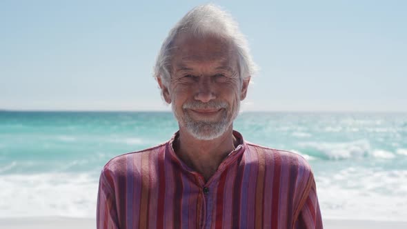 Senior man standing on the beach and looking at camera