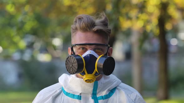 Portrait of a Young Man in a Protective Suit, Respirator and Gloves Looks Into the Camera, Puts on