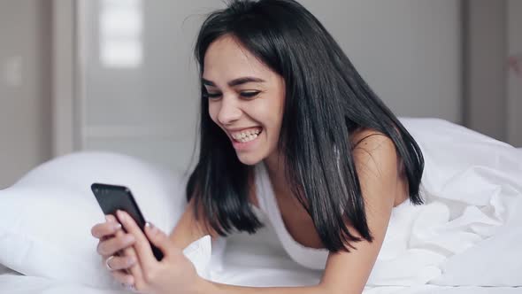 Pretty Girl in Bed Reads Messages on Smartphone and Smiles