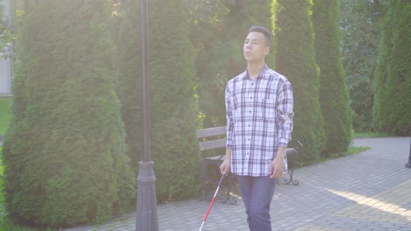 Young Visually Impaired Asian Man with a Cane Is in the Park