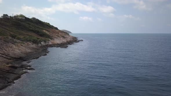 Aerial: landscape view of a rocky beach a small hill on the left side , with waves coming from the o