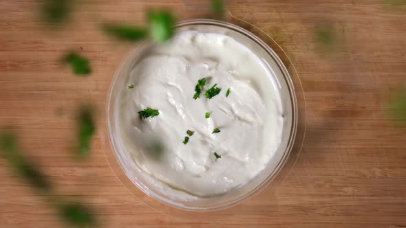 Top view of chopped greens falling into bowl of yoghurt.