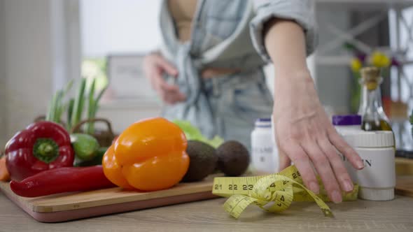 Table with Healthful Vegetables and Vitamins and Female Hand Putting Measuring Tape