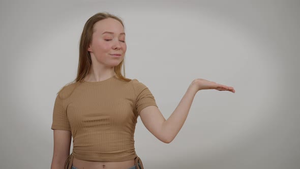 Confident Slim Woman Advertising at Grey Background Gesturing Hand Palm Up Smiling Looking at Camera