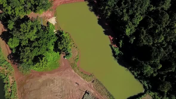 Aerial bird's eye view rising up over a small fishing pond on a fish farm in rural Brazil