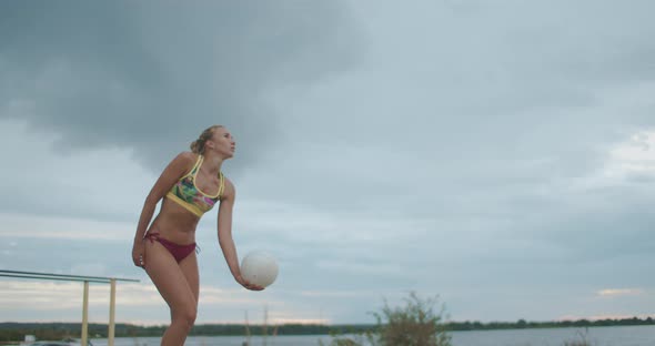 Slim and Active Sportswoman Is Playing Beach Volleyball at Nature, Slow Motion Shot Against Cloudy