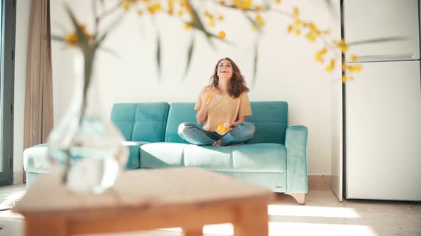 A Young Beautiful Woman Juggling with Three Oranges While Sitting on the Couch