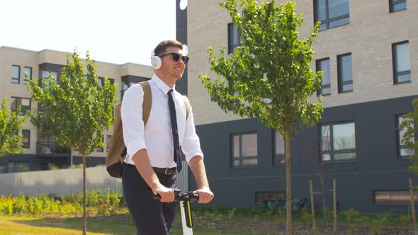 Businessman with Headphones Riding Scooter in City