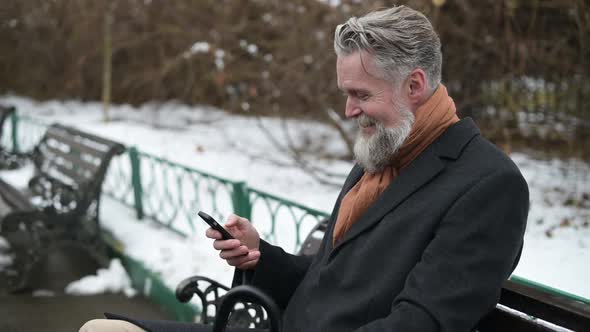 Gray-haired man sits on a park bench texting on the phone, then answers the call