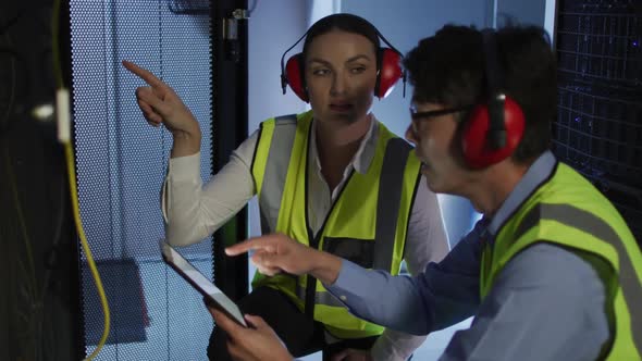 Diverse female and male it technicians wearing headphones using tablet checking computer server
