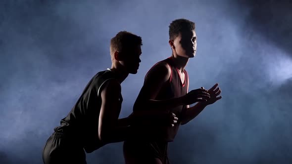 Two Young Athletes Practice Basketball in a Dark Smoky Studio Under the Spotlight