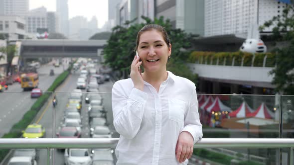 Young Woman Talks on White Smartphone and Smiles Cheerfully