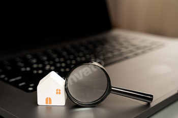 House and magnifying glass on laptop keyboard.