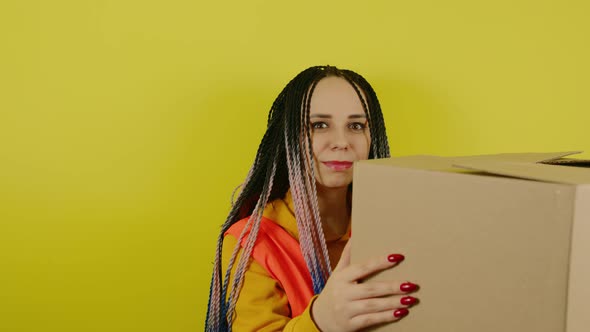 Young Woman in Vest with Cardboard Box on Yellow Background in Studio