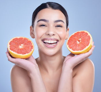 Portrait of a happy mixed race woman holding a grapefruit. Hispanic model promoting the skin benefi