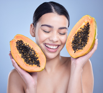 A happy smiling mixed race woman holding a papaya. Hispanic model promoting the skin benefits of a