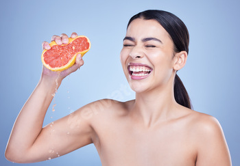 A  happy mixed race woman holding a grapefruit. Hispanic model promoting the skin benefits of citru