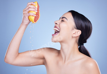 A  happy mixed race woman holding a grapefruit. Hispanic model promoting the skin benefits of citru