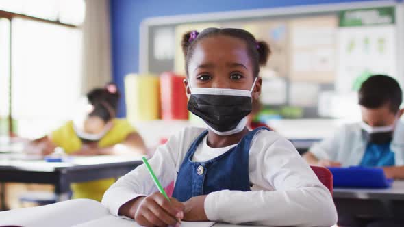 Portrait of african american schoolgirl wearing face mask in classroom looking at camera