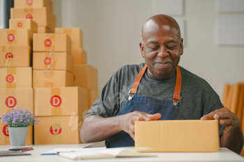 Man in apron packing boxes at a table, surrounded by boxes.